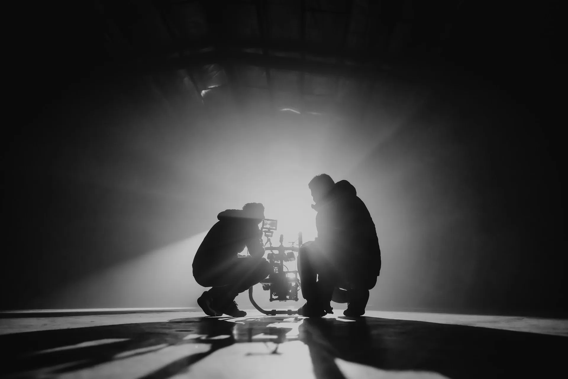 Two filmmakers crouched over a camera rig in a beam of studio light